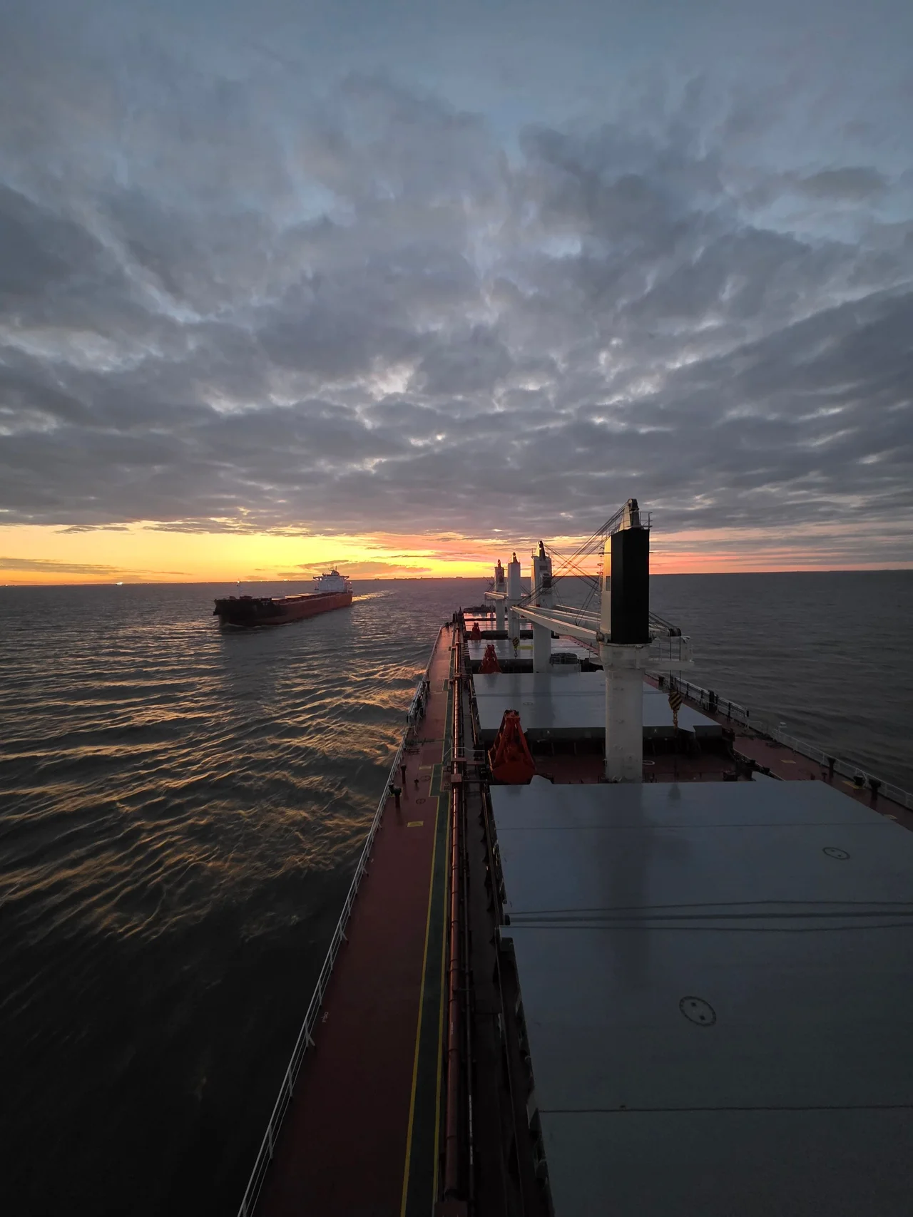 The view from a cargo vessel towards another ship at sunset